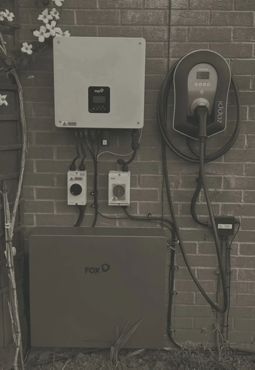 A Fox ESS inverter and battery on a brick wall, with an EV charger beside them
