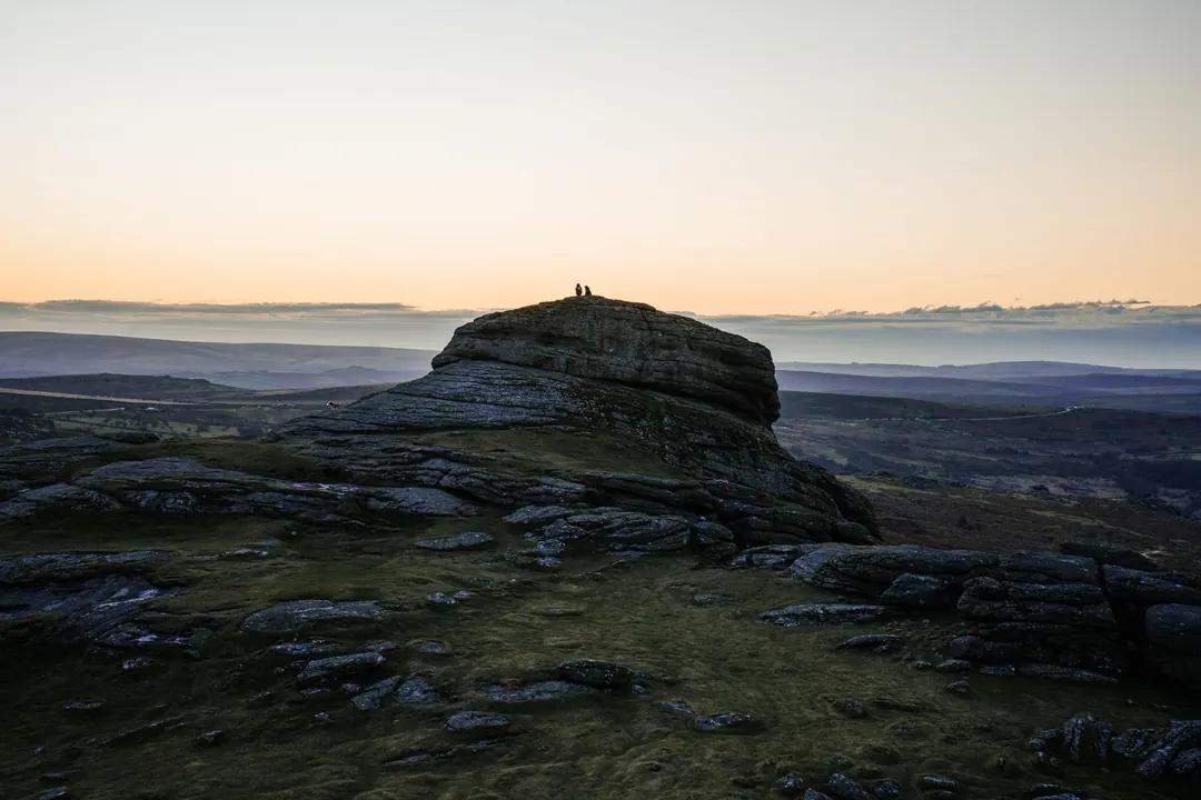 Haytor, a granite tor on Dartmoor, at sunset, with two people standing on its summit