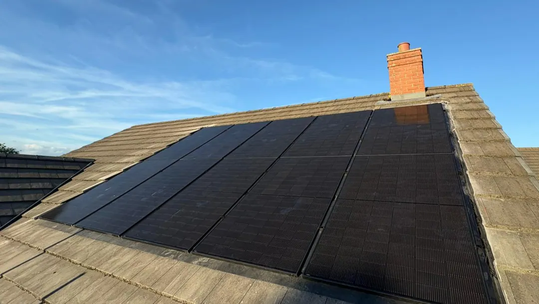 Black solar panels covering most of a concrete-tiled roof slope, a red-brick chimney above them
