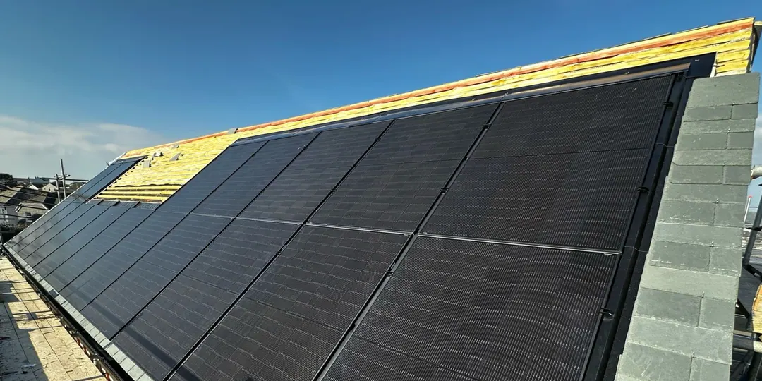 An all-black solar array set into a roof that is still being finished, beside a grey blockwork gable
