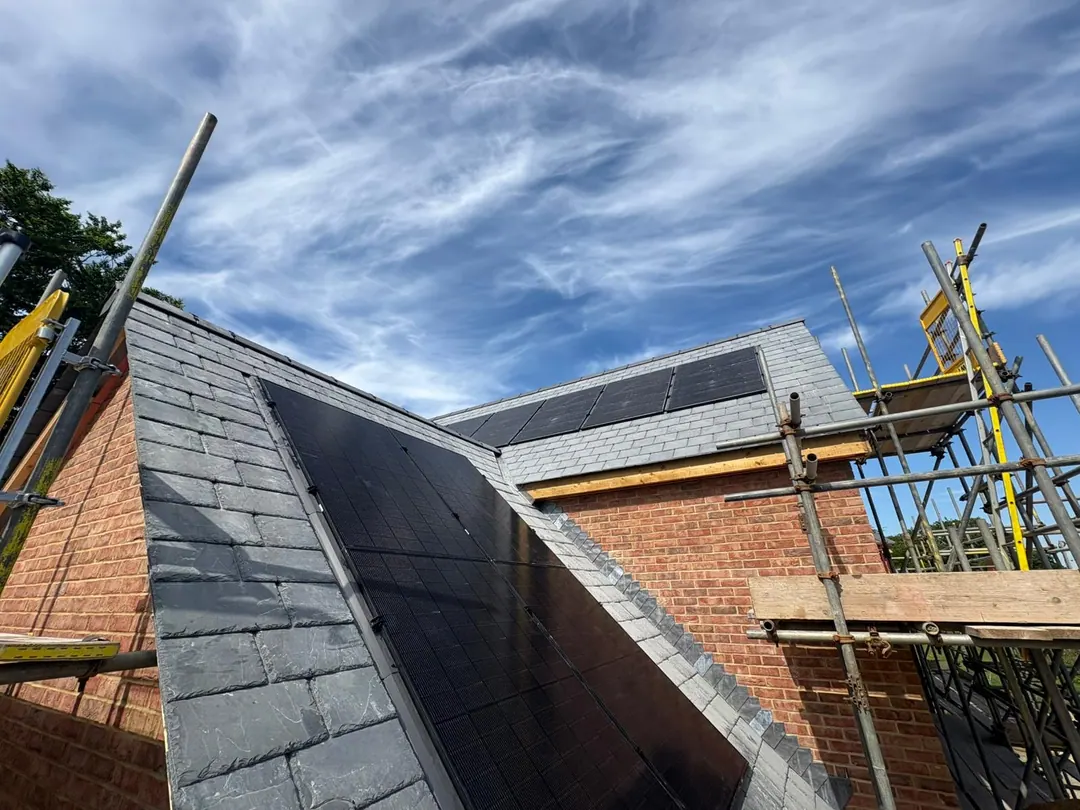 A brick house with an all-black in-roof solar array on its slate roof, the scaffold still up
