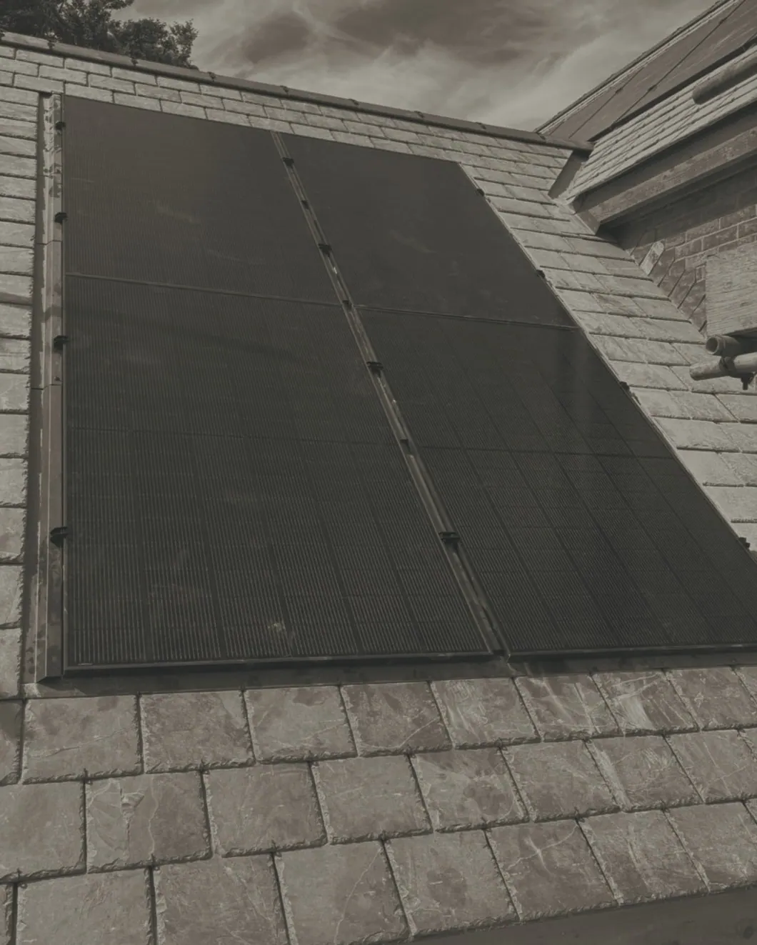 Four black panels sitting flush among the slates, seen from the scaffold, with a brick gable to the right