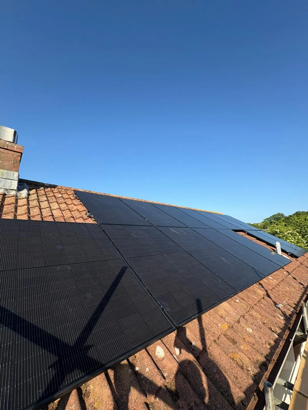 Black solar panels on a clay-tiled roof under a clear blue sky, seen from the access ladder